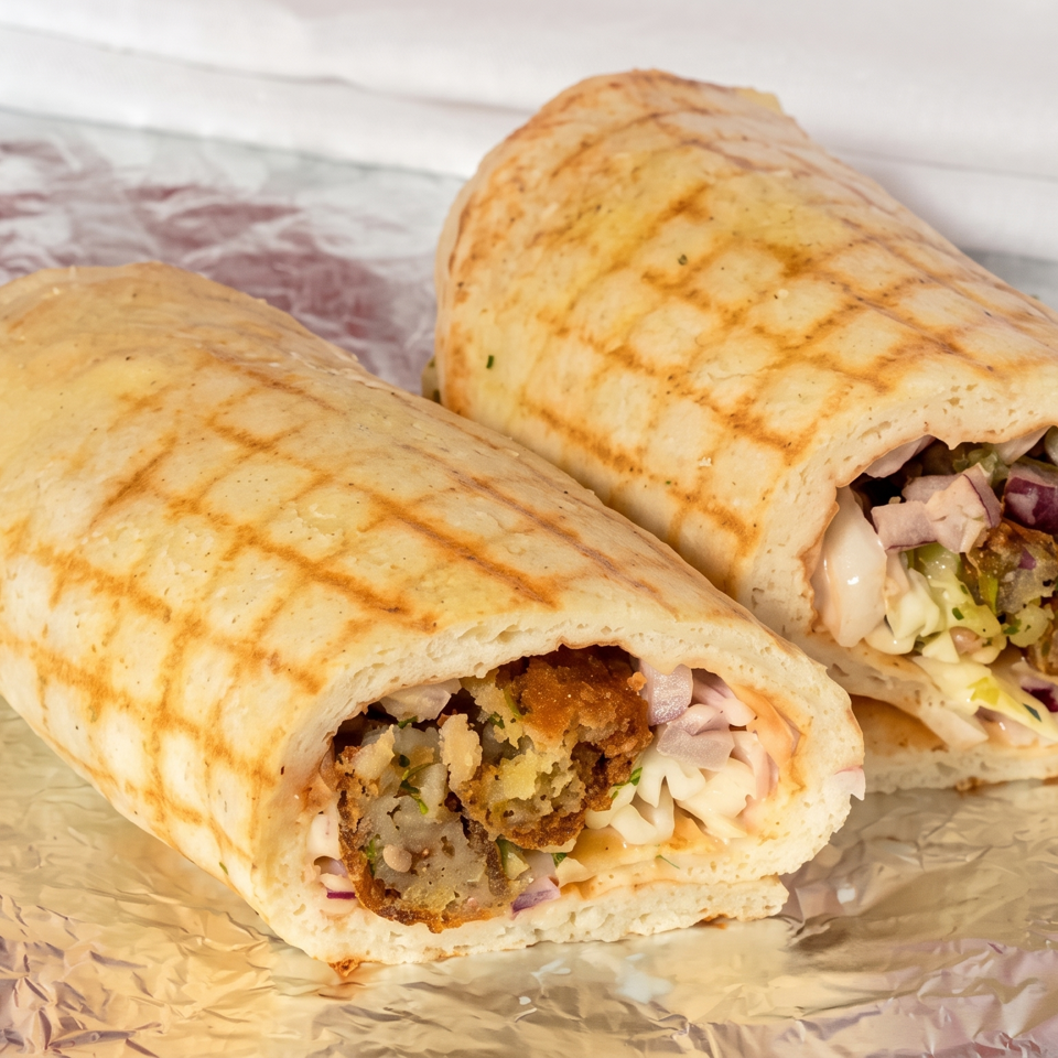 Two grilled flatbread wraps filled with falafel, lettuce, onions, and creamy sauce on foil.