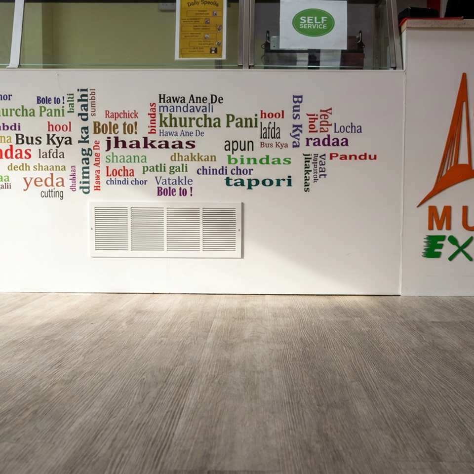 Mumbai Express restaurant counter featuring colorful Indian phrase typography, self-service signage, drinks, and a Mumbai skyline logo.