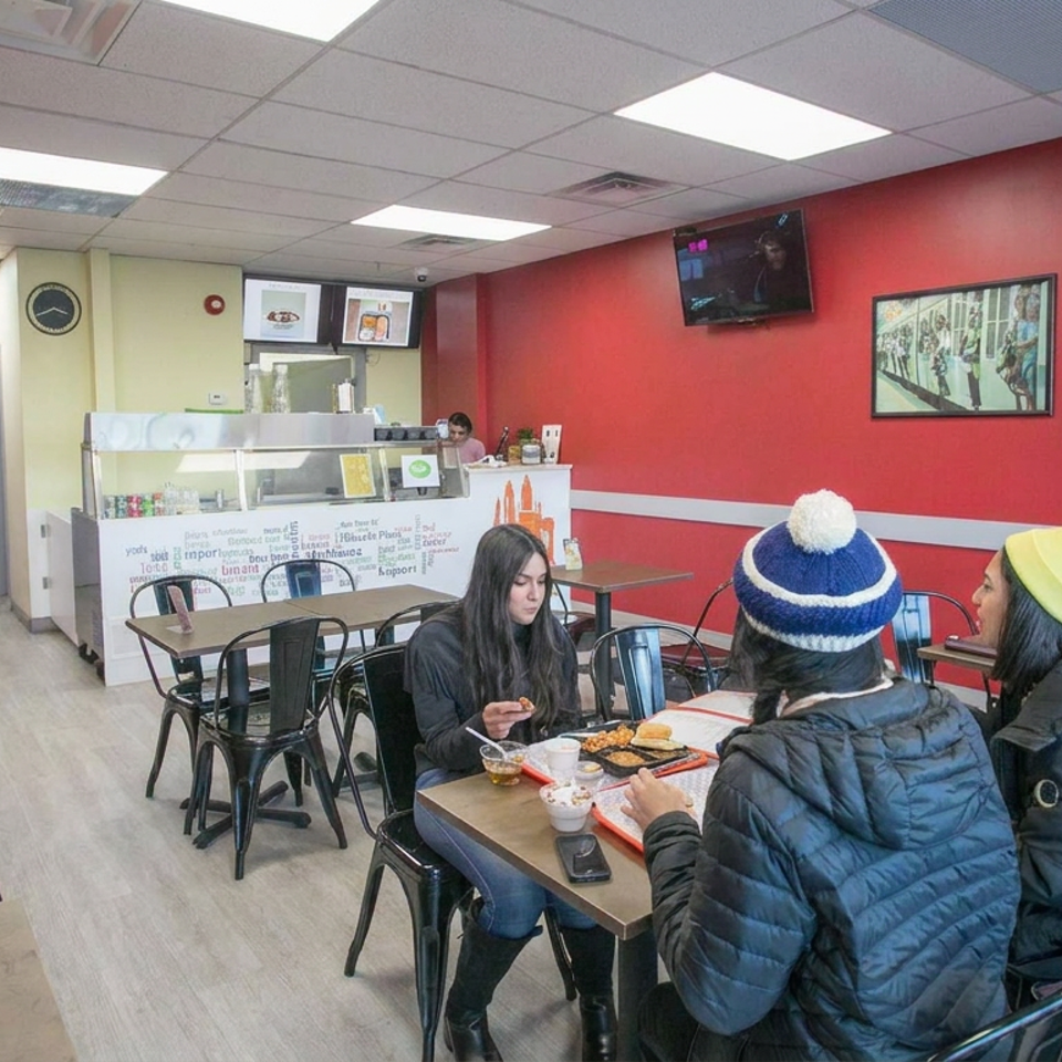 Casual restaurant interior with red walls, framed artwork, counter service, and three diners sharing a meal at a table.