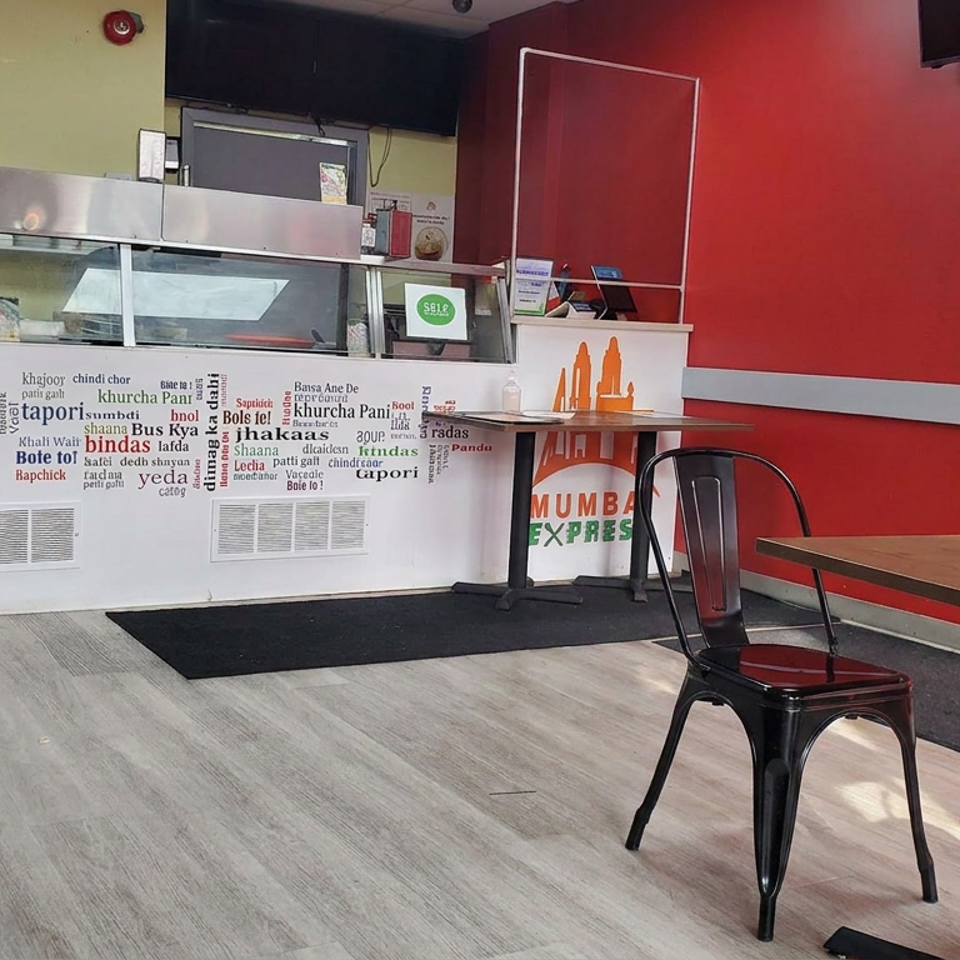 Bright Mumbai Express restaurant interior with a service counter, red accent walls, metal chairs, and wooden tables.